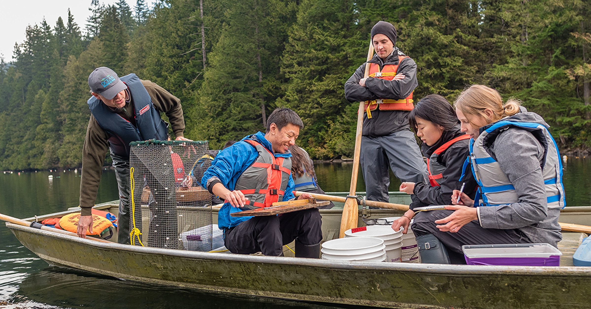 5 UBC researchers are on a boat. They are looking at fish they just caught for their research.